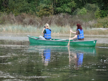 two women in blue lifejackets paddling in a canoe