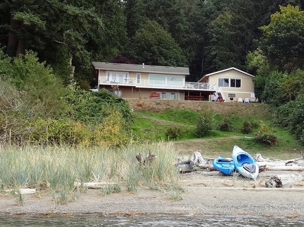 water with kayaks on beach and a house on a hill in the background