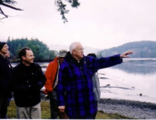 Man pointing out at a body of water with adults behind him looking out to the water